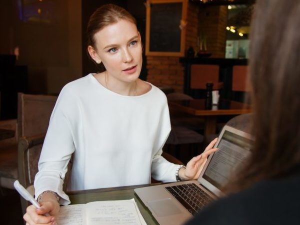 Eine Frau hört einer nicht eindeutig erkennbaren weiteren Person zu und macht Notizen zum Gespräch.